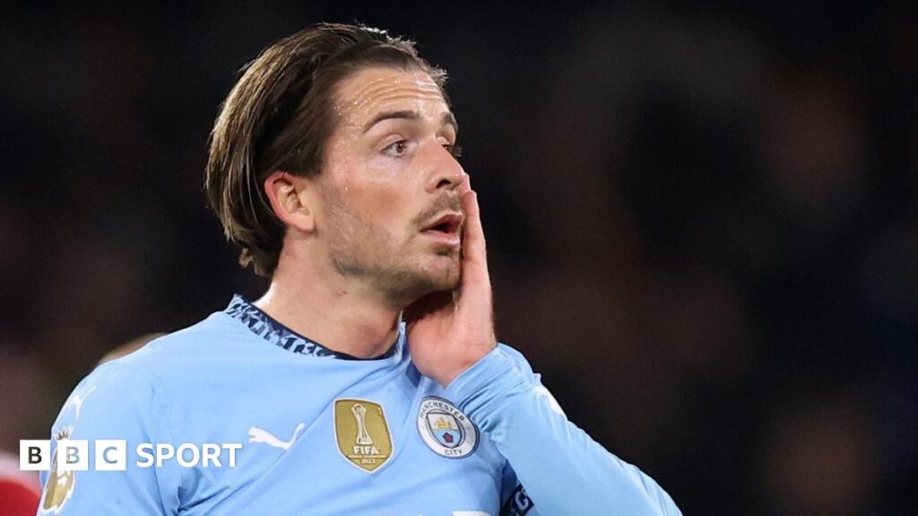 Jack Grealish in Manchester City kit with his left hand raised to his face