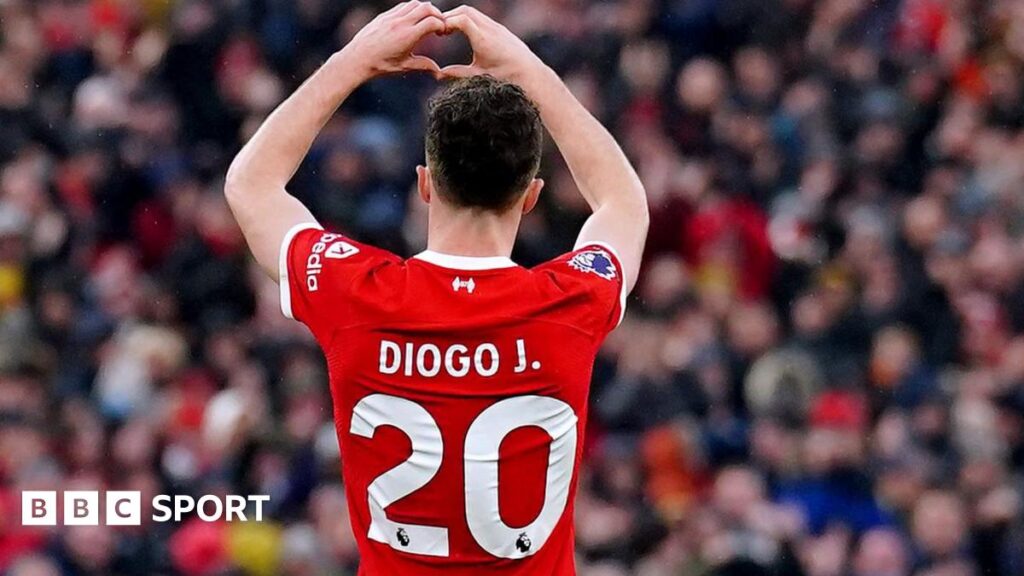Diogo Jota makes a heart shape with his hands with his back to the camera so his number 20 shirt is visible