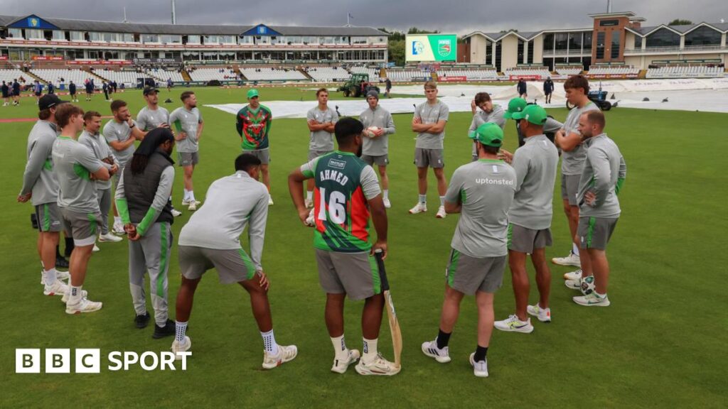 Leicestershire players in a huddle with covers on the pitch behind