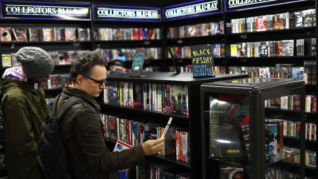 Two people in a video store browsing 4K Blu-rays from multiple shelves