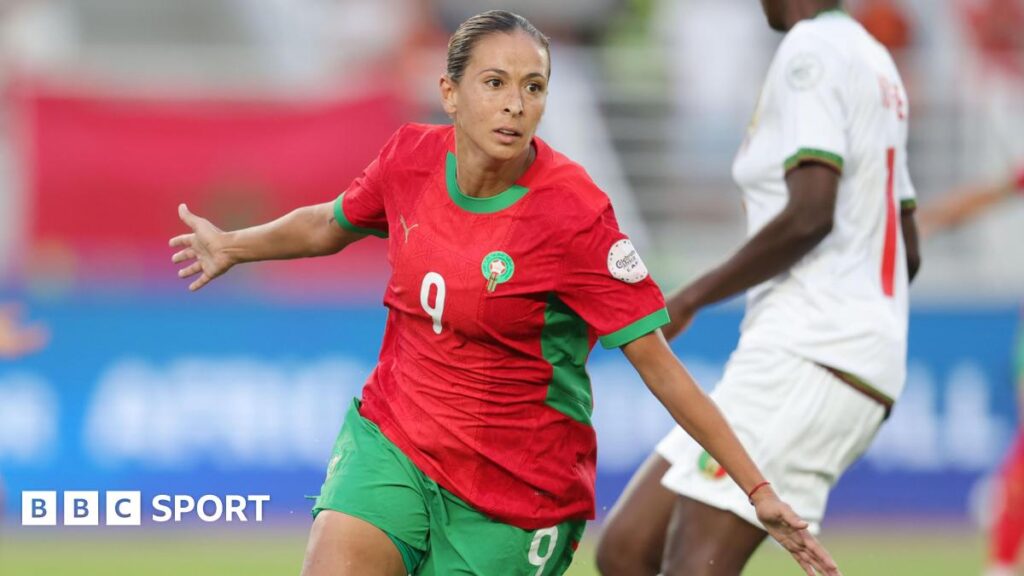 Ibtissam Jraidi in red Morocco shirt and green shorts spreads her arms to her sides and wheels away in celebration as a Mali player in white is seen in the background