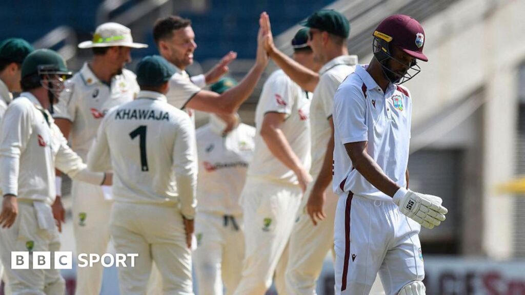 Roston Chase walking off after being dismissed, with Australia players celebrating in the background.