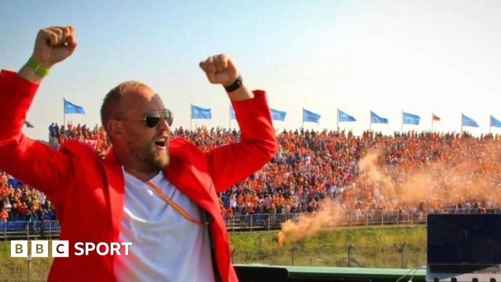 Rick Jansen DJs for the crowds at Zandvoort. Orange smoke from flares can be seen in the background, while Rick is wearing an orange jacket and is lifting his arms in the air