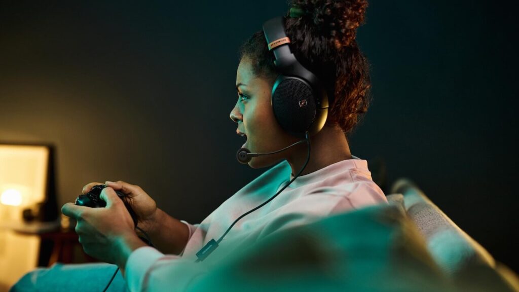 A young woman with dark hair wearing a pair of Sennheiser HD headphones and playing a video game
