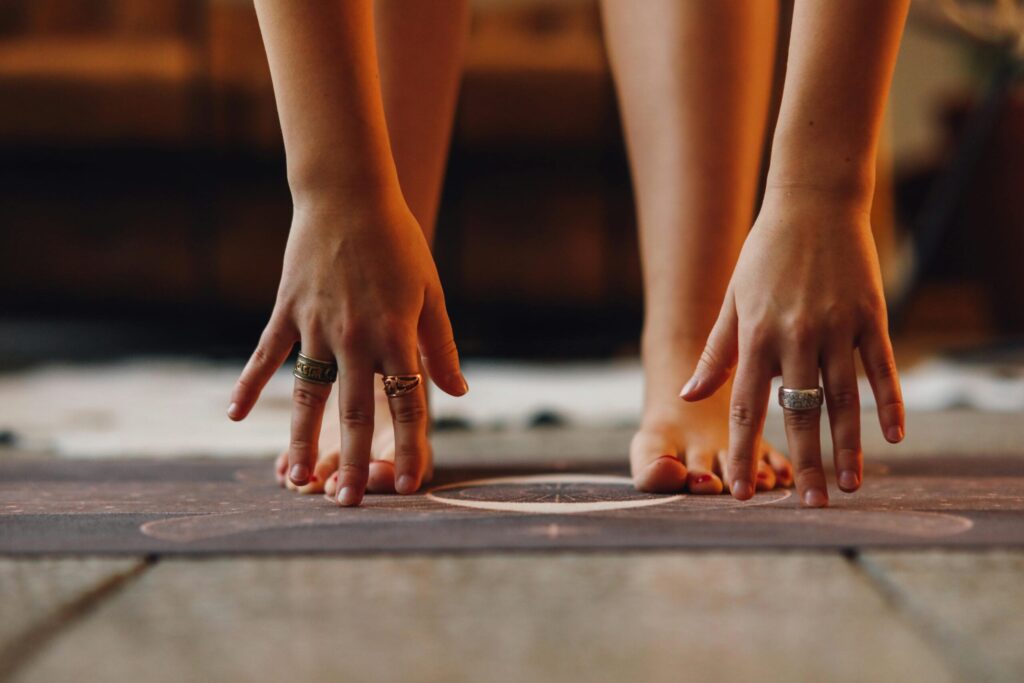 Image of woman's hands reaching toward her feet on yoga mat.