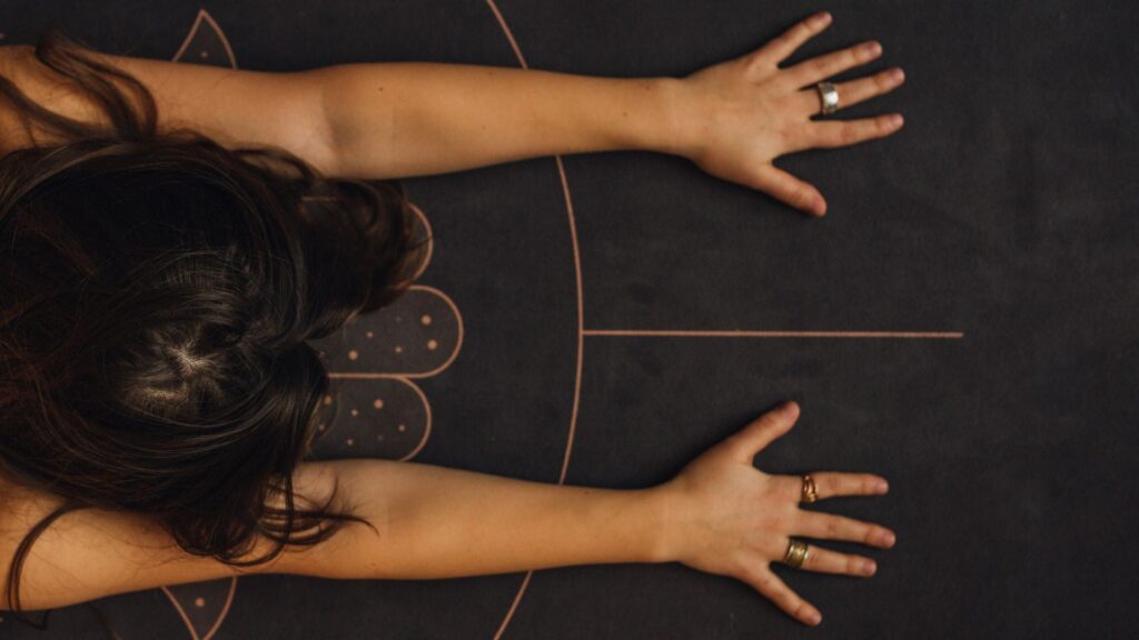 Aerial shot of a woman in Child's Pose with a close-up on her hands and wrists.
