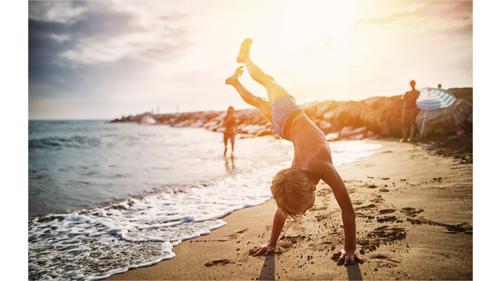 Little boy on a beach with the late afternoon sun behind him learning how to do Handstand