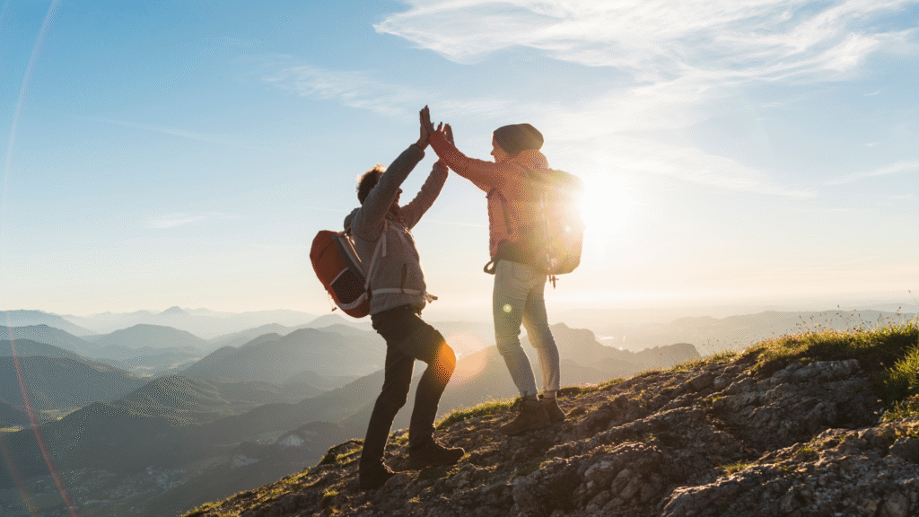 Two people high fiving at the top of a hill on a hike