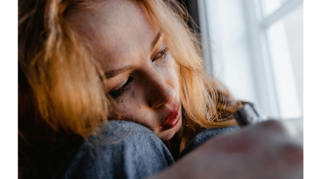 This Yoga Teaching Transforms Your Struggles Into Strength Woman sitting on a window seat with her knees drawn to her chest looking outward with tears on her face and smudged mascara while working on tapas in yoga