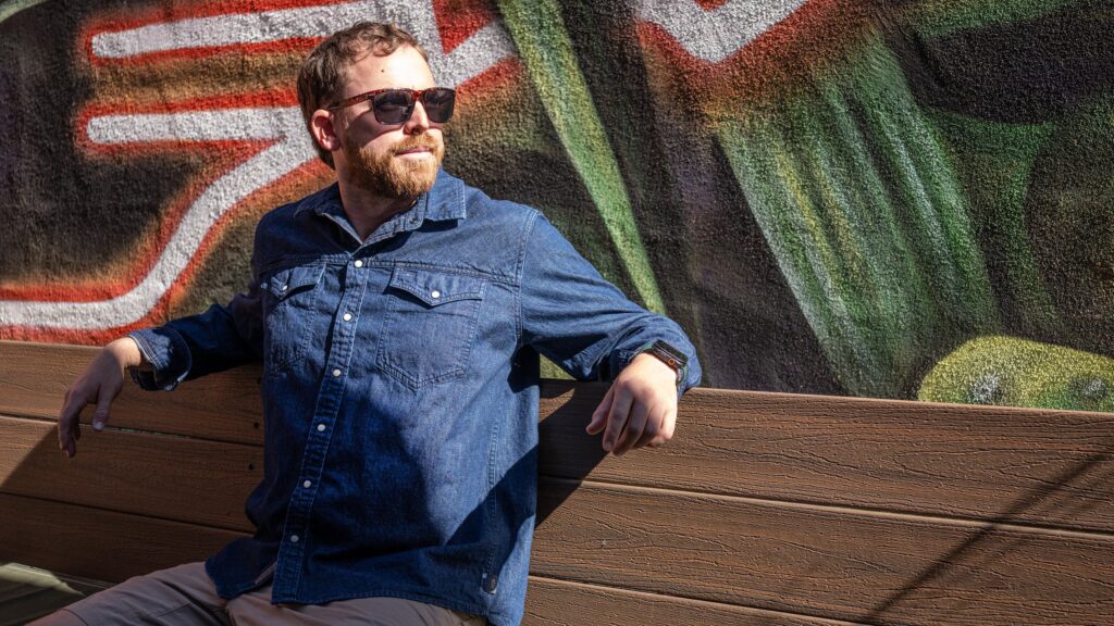 Our 3 Favorite Denim Shirts man in denim shirt sitting on bench in front of a colorful southwestern blanket