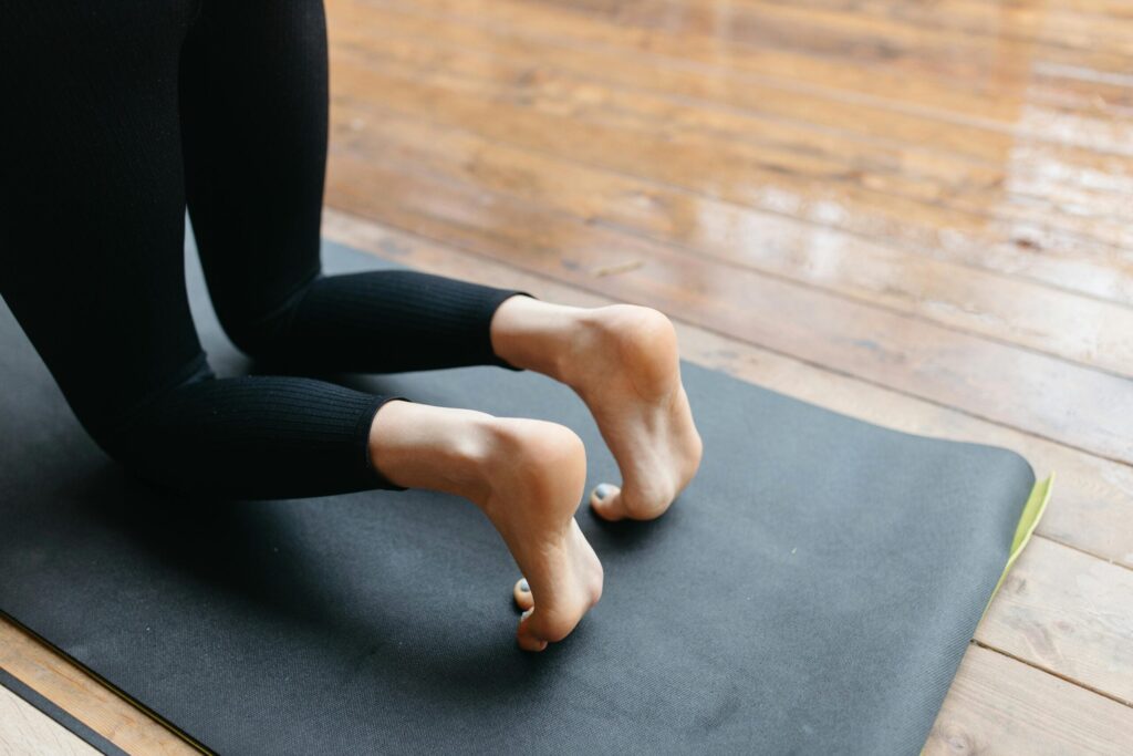 What I Learned From One of My Most Challenging Yoga Poses Image of woman on knees on black yoga mat. Her toes are tucked and she's wearing black leggings.